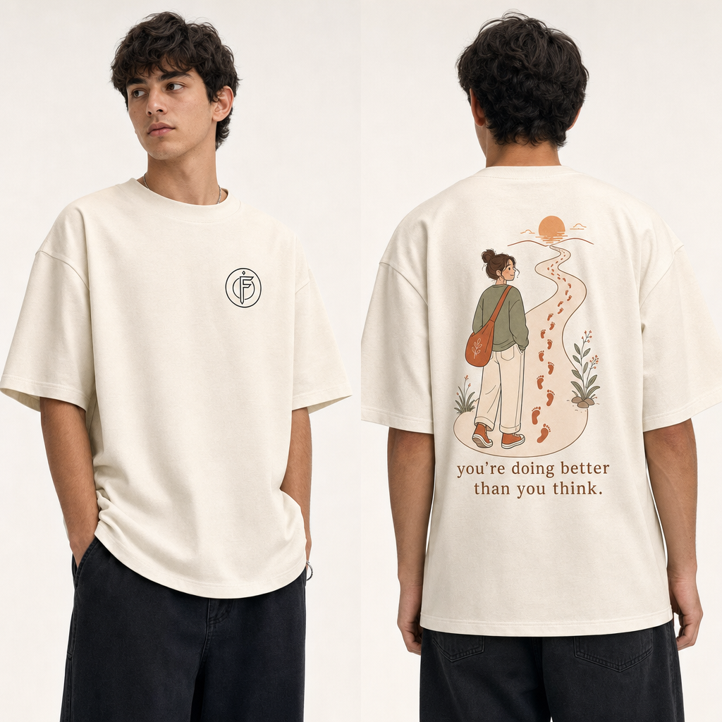 Editorial studio photo of a model wearing an oversized off-white heavyweight t-shirt with a graphic reading YOU ARE DOING BETTER THAN YOU THINK, relaxed streetwear fit, clean studio background.