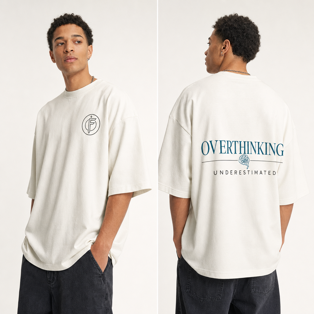 Editorial studio photo of a model wearing an oversized heavyweight t-shirt with an OVERTHINKING, UNDERESTIMATED graphic, front and back views, relaxed streetwear fit, clean studio background.